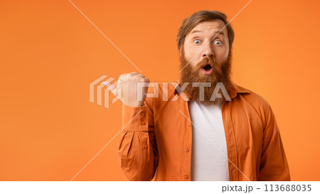 Surprised redhaired man with beard pointing thumb finger aside, studio Surprised redhaired man with beard pointing thumb finger aside, studio 113688035