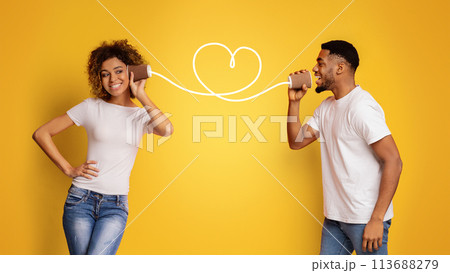 Young black couple with can phone on orange background Young black couple with can phone on orange background 113688279
