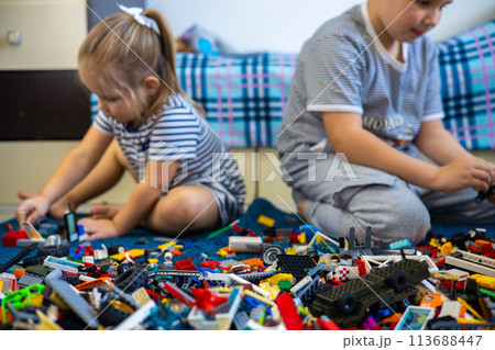 Children brother and sister are sitting among Lego constructors and collecting toys. Children enthusiastically play with Legos while sitting on the floor and collect their toys. 113688447