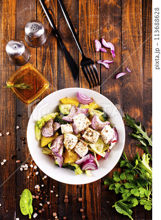 Greek salad of fresh cucumber, tomato, sweet pepper, lettuce, red onion, feta cheese and olives with olive oil. Healthy food, top view Greek salad of fresh cucumber, tomato, sweet pepper, lettuce, red onion, feta cheese and olives with olive oil. Healthy food, top view 113688628