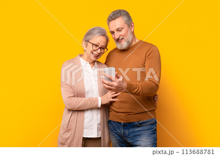 Happy mature gray couple looking at smartphone screen hugging, studio Happy mature gray couple looking at smartphone screen hugging, studio 113688781