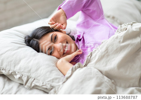 Relaxed woman laying on bed in purple pajama Relaxed woman laying on bed in purple pajama 113688787