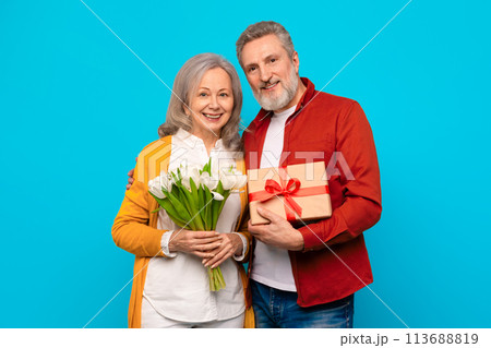 Happy senior couple posing with present and bouquet in studio 113688819