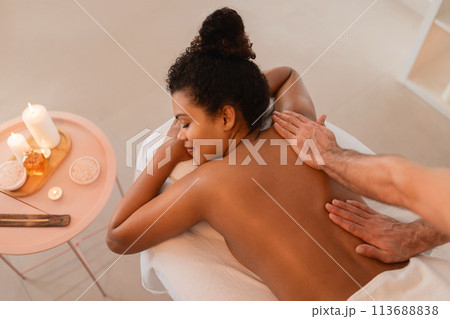 Woman enjoying a massage in a candlelit room Woman enjoying a massage in a candlelit room 113688838