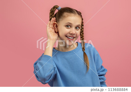 Girl gesturing to listen with hand to ear on pink Girl gesturing to listen with hand to ear on pink 113688884