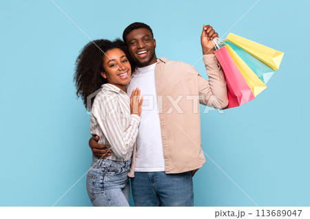 Happy couple hugging with shopping bags on blue background Happy couple hugging with shopping bags on blue background 113689047