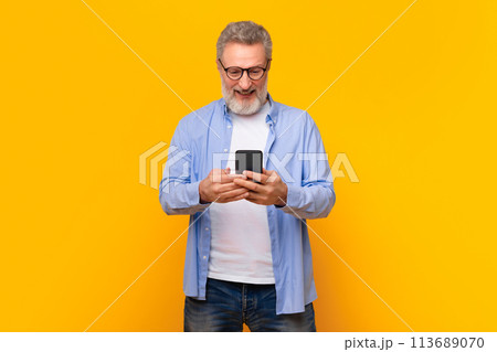 Cheerful mature gray haired man texting via smartphone, yellow background 113689070