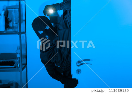Burglar with flashlight opening a door stealthily Burglar with flashlight opening a door stealthily 113689189
