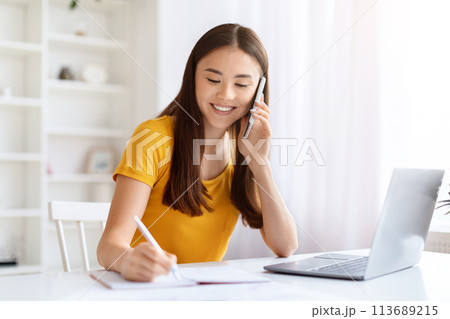 Woman on phone writing notes with laptop open Woman on phone writing notes with laptop open 113689215