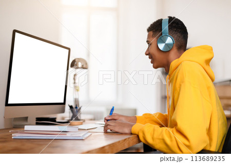 Black teen guy studying with headphones and computer at desk 113689235