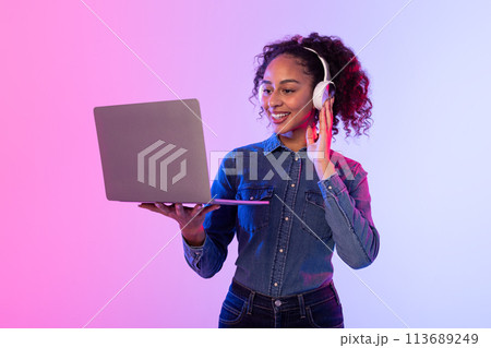 Woman in denim holding laptop with headphones Woman in denim holding laptop with headphones 113689249