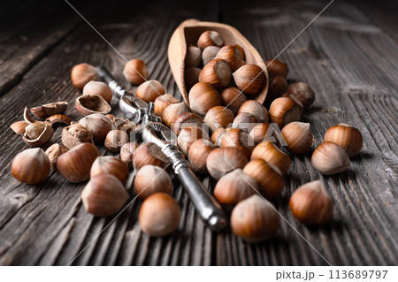 Whole and cracked hazelnuts with a classic silver nutcracker 113689797