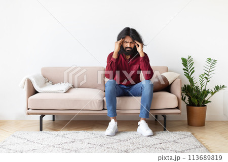 Man with headache sitting on couch at home 113689819