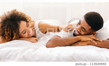 Cheerful woman touching her husband nose in bed Cheerful woman touching her husband nose in bed 113689940