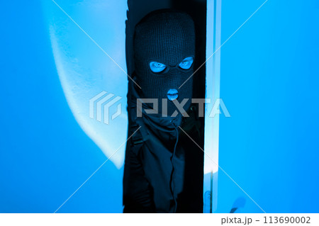 Masked intruder man peeking inside room suspiciously Masked intruder man peeking inside room suspiciously 113690002