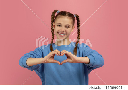 Girl making heart shape with hands on pink backdrop Girl making heart shape with hands on pink backdrop 113690014