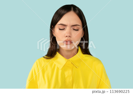 Upset emotional young woman, with eyes closed showing a vulnerable moment of sadness at blue studio background Upset emotional young woman, with eyes closed showing a vulnerable moment of sadness at blue studio background 113690225