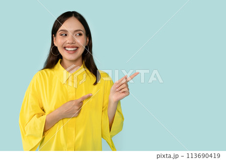 Happy Young Woman Pointing Aside At Copy Space on Blue Background Happy Young Woman Pointing Aside At Copy Space on Blue Background 113690419