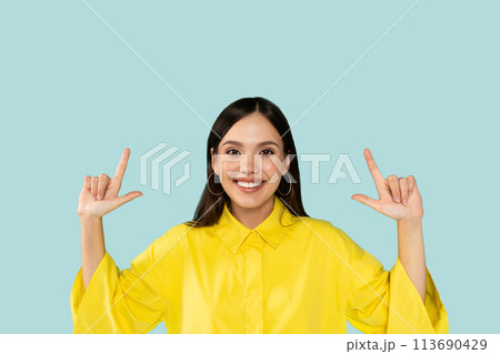 Happy cheerful beautiful young latin woman pointing up at blue studio background 113690429