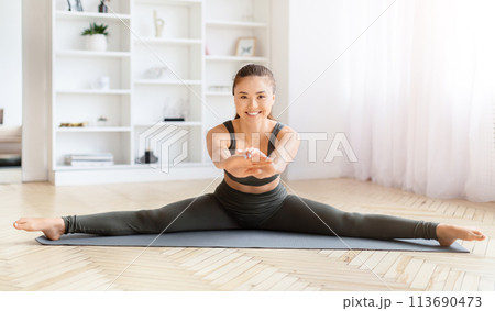 Woman performing a split stretch on yoga mat Woman performing a split stretch on yoga mat 113690473