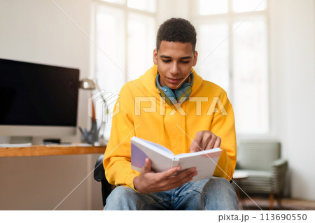 Young man reading a notebook at a home office desk Young man reading a notebook at a home office desk 113690550