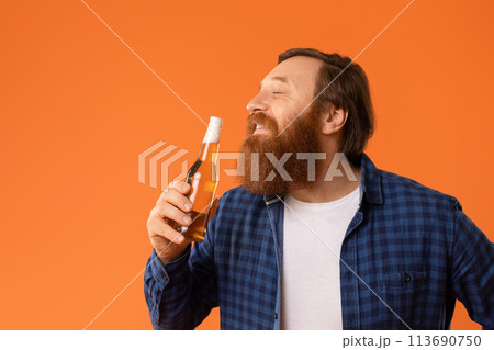Contented redhaired bearded man enjoys beer posing with bottle, studio Contented redhaired bearded man enjoys beer posing with bottle, studio 113690750