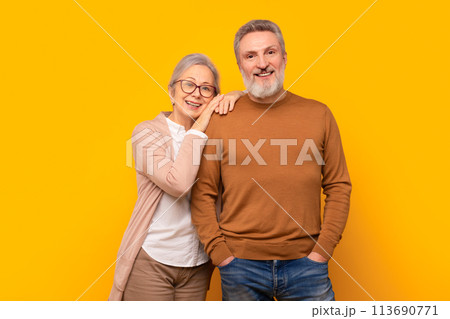 Happy Caucasian elderly couple embraces against yellow studio backdrop Happy Caucasian elderly couple embraces against yellow studio backdrop 113690771