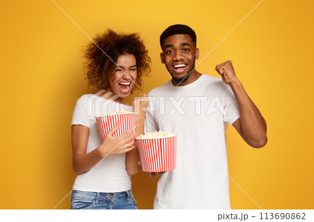 Emotional black couple enjoying movie with buckets of popcorn 113690862