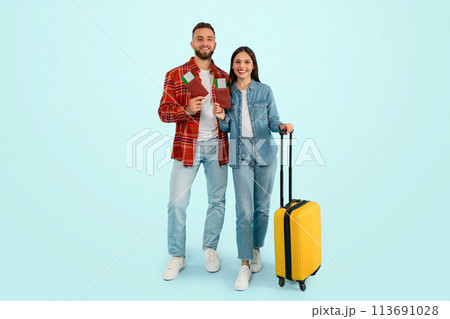 Cheerful caucasian travelers couple standing with tickets and suitcase, studio Cheerful caucasian travelers couple standing with tickets and suitcase, studio 113691028