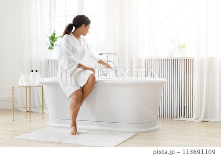 Woman preparing for a bath in bright room Woman preparing for a bath in bright room 113691109