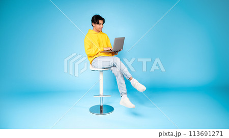 Teen using laptop on stool with focused look 113691271