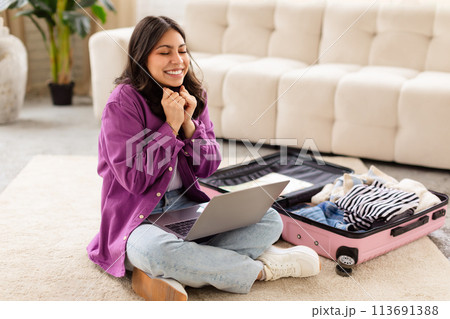 Smiling woman with laptop and open suitcase 113691388