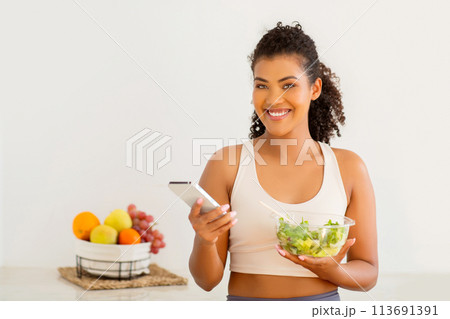 Happy woman browses recipe app on her smartphone in kitchen 113691391