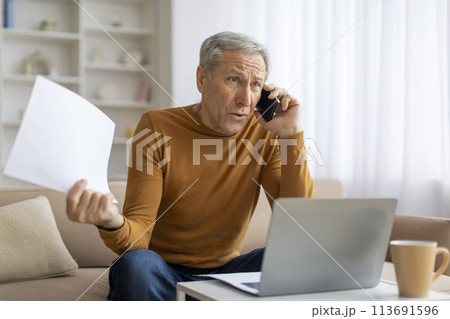 Man multitasking with phone, laptop, and papers 113691596