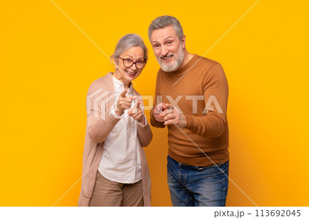 Joyful senior couple in casual pointing fingers at camera, studio Joyful senior couple in casual pointing fingers at camera, studio 113692045