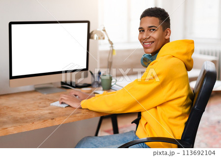 Smiling black teen guy at computer desk with blank screen 113692104