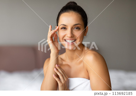Happy woman looks at the camera touching face gently indoor Happy woman looks at the camera touching face gently indoor 113692185