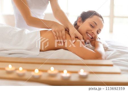 Happy woman lies as masseuse making soothing back massage indoor Happy woman lies as masseuse making soothing back massage indoor 113692359