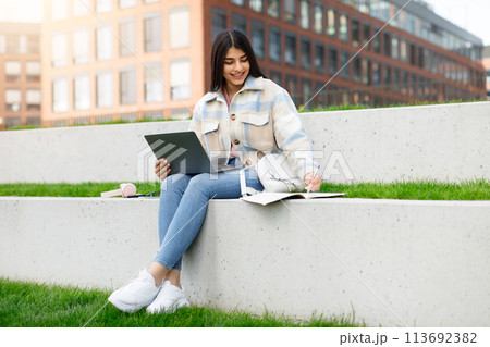 Student with laptop and notebook studying outside Student with laptop and notebook studying outside 113692382