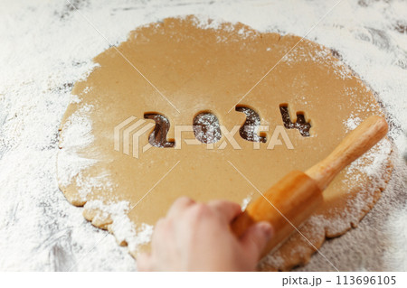 raw dough with 2024 numbers cut from rolled cookie on flour with woman's hand 113696105