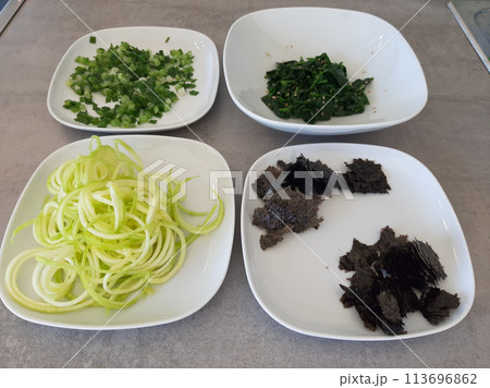 Homemade side dish with spinach, zucchini spirals, spring onions and chopped nori algae served on white plates 113696862