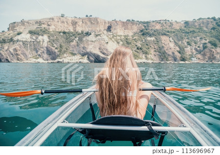 Woman in kayak back view. Happy young woman with long hair floating in transparent kayak on the crystal clear sea. Summer holiday vacation and cheerful female people relaxing having fun on the boat 113696967