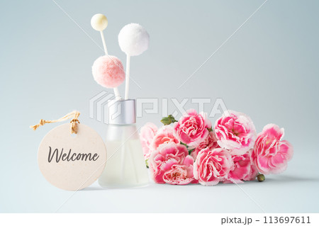 Fragrance diffuser with welcome tag and pink flowers on vintage blue background 113697611