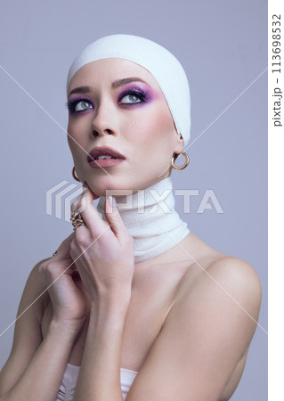 Portrait of young beautiful woman in elegant hair accessories, bandage, golden earrings with bright makeup posing on light purple background Portrait of young beautiful woman in elegant hair accessories, bandage, golden earrings with bright makeup posing on light purple background 113698532