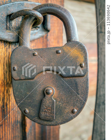 The old 90 years age rusty padlock hanging on hinges. Close-up The old 90 years age rusty padlock hanging on hinges. Close-up 113698642