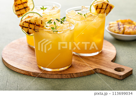 Grilled pineapple margarita garnished with lime wedges 113699034