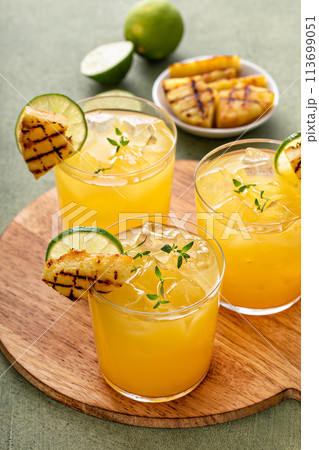 Grilled pineapple margarita garnished with lime wedges 113699051