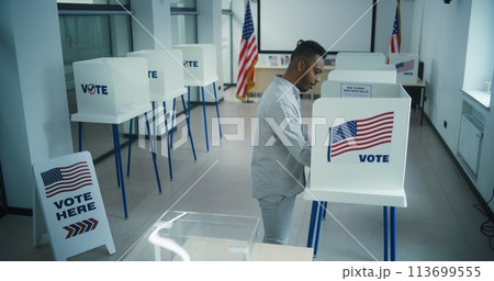 African American man votes in voting booth, then puts ballot in box 113699555