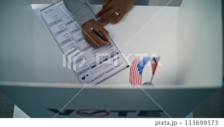 African American US citizen filling out paper ballot in voting booth 113699573