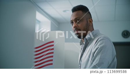 African American man fills out paper ballot in voting booth, than smiles and looks straight African American man fills out paper ballot in voting booth, than smiles and looks straight 113699586